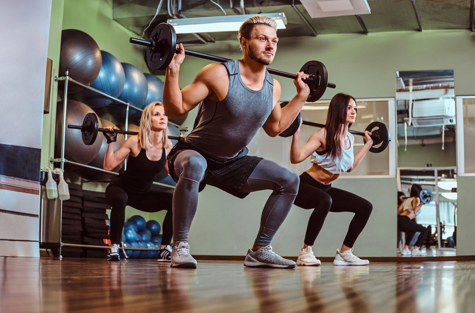 Group of people exercising with barbell doing squats in a fitness club.
